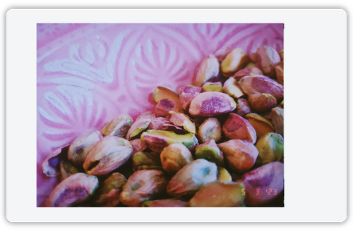 A zoomed in photo of pistachios in a pink bowl. 